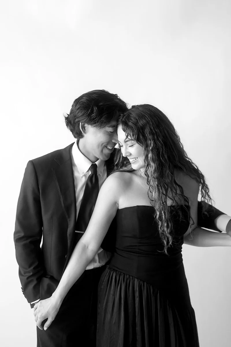 A couple smiling with their foreheads together in a black and white portrait.