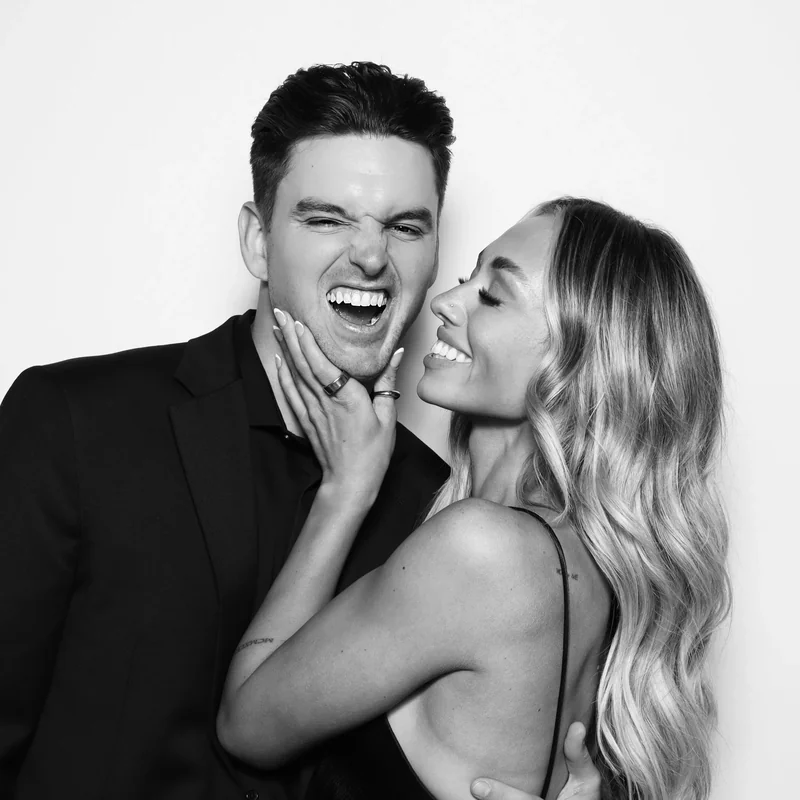 A couple laughing together in a black and white photo booth portrait.