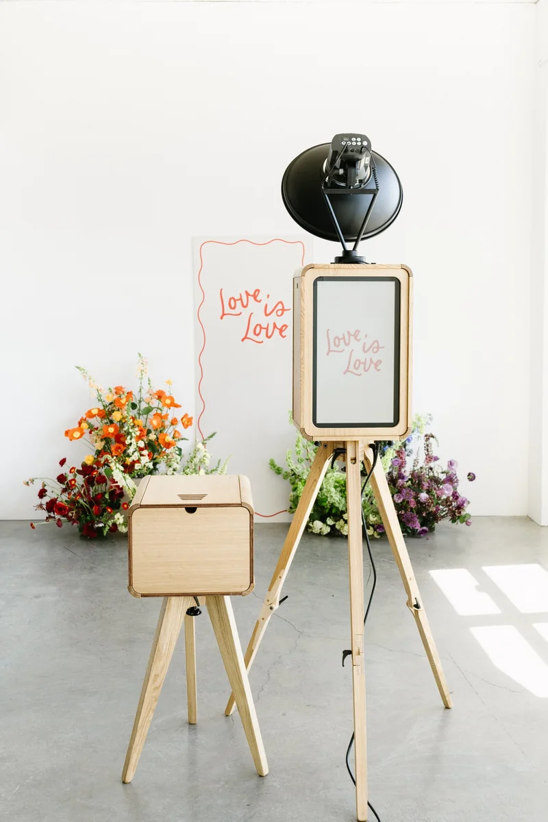 The wooden Icon Booth and matching printer beside colourful flowers in a sunlit white room.